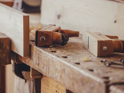 Werkbank mit Holz und verschiedenen Handwerkzeugen, darunter Hobel und Holzspäne.