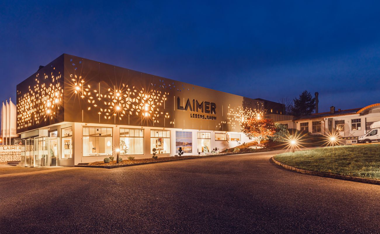 Moderne Gebäude mit beleuchteter Fassade und stilvollem Design, umgeben von einer gepflegten Landschaft bei Nacht.