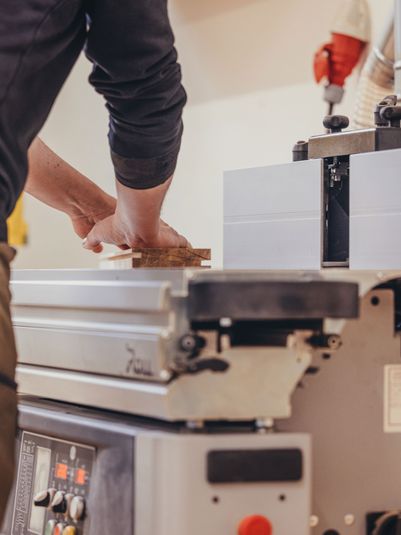 Ein Handwerker bearbeitet Holz an einer Maschinenfräse in einer Werkstatt.