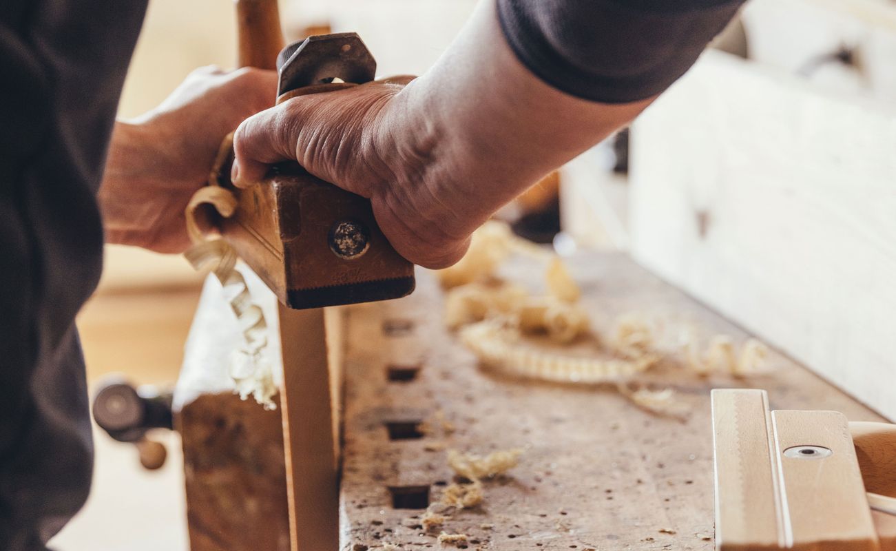 Ein Handwerker benutzt eine Hobelmaschine, um Holz zu bearbeiten. Späne liegen auf der Werkbank.